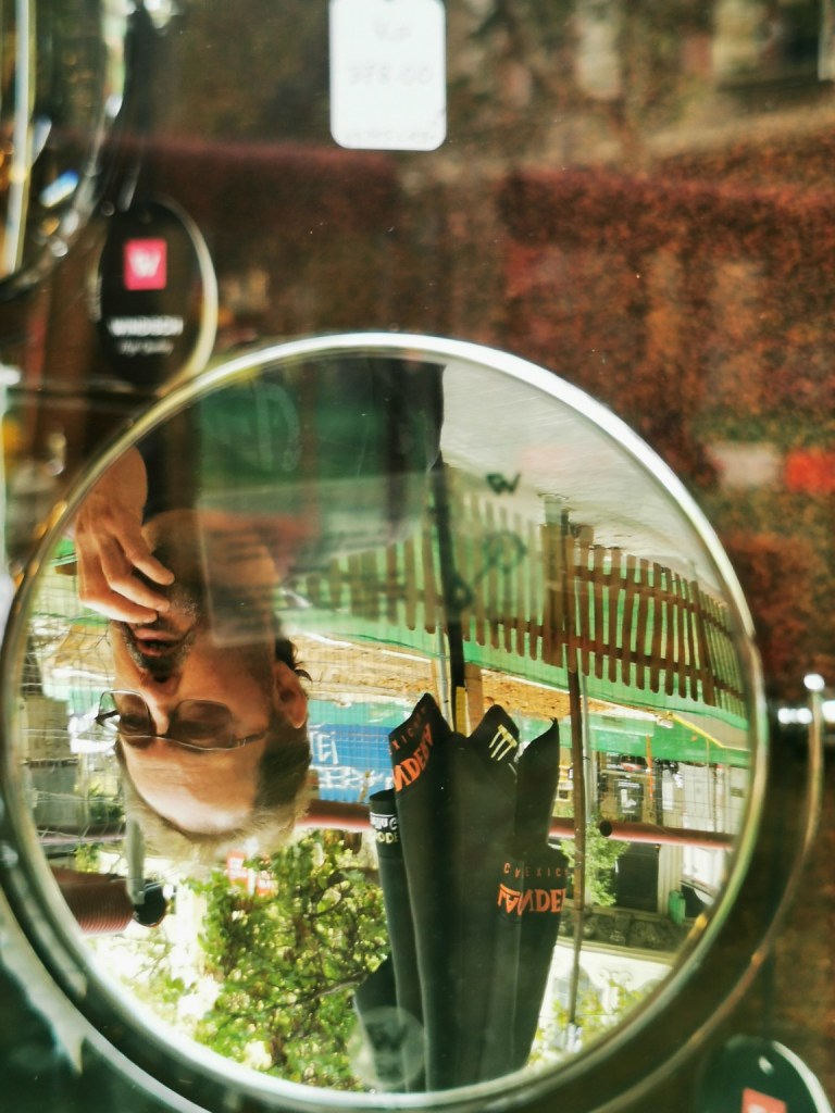 Persona sentada en la terraza de una cafetería vista a través de un espejo de un escaparate. Reflejo