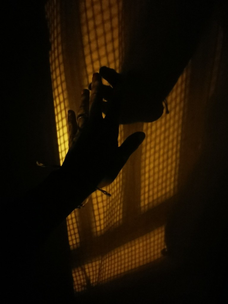 Manos extendidas hacia la luz que que entra por una ventana y proyecta sombras en la pared.